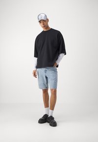 Čierne oversized tričko, svetlo modré deninové šortky, čierne topánky, biele ponožky a strieborná čiapka. Neformálny outfit s voľným strihom.