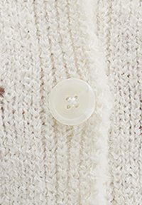 Cream-colored knitted cardigan with a soft texture, featuring a round, clear plastic button with four holes and visible stitching details.