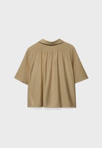 Beige Kurzarmbluse mit gerafftem Rücken, weitem Kragen und lockerem Schnitt vor einem schlichten hellen Hintergrund.