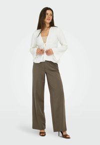 Top blanc à rayures, avec des manches évasées, noué à la taille, associé à un pantalon olive vert ample à taille haute et des talons ouverts.