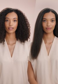 Twee afbeeldingen naast elkaar van dezelfde persoon: links met volumineus, krullend zwart haar; rechts met stijl, glanzend zwart haar. Beiden dragen een licht beige top.