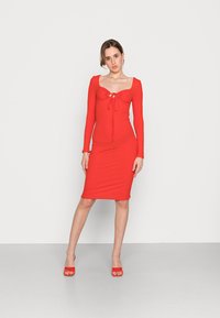 Vestido justo de manga longa vermelho com decote quadrado, detalhes plissados e frente com cordão. Textura suave, comprimento até ao joelho, design ajustado.