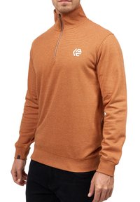 Orange zip-up sweatshirt med høj krave, struktureret stof, lange ærmer og et hvidt logo på brystet. Har ribbet kant og manchetter.
