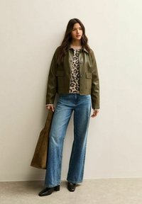 Olijfgroene cropped nep leren jasje, beige panterprint sweater, brede blauwe jeans en zwarte haklaarzen met een bruine tas.