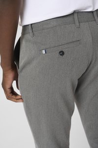 Grijze, gestructureerde broek met een achterzak die een zwarte knop en een klein blauw-wit gestreept accent heeft. De tailleband is op maat gemaakt.