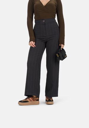 Pantalons larges à rayures noires avec une taille haute, associés à un top marron à manches longues et des baskets à imprimé animal. Petite pochette noire.