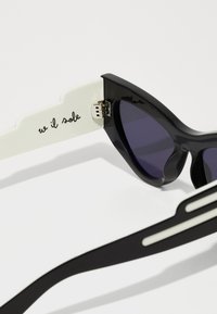 Μαύρα γυαλιά ηλίου τύπου cat-eye με σκούρους φακούς και λευκές λεπτομέρειες στα άκρα. Διαθέτουν ασημένιους μεντεσέδες και το κείμενο "w il sole" στο εσωτερικό.
