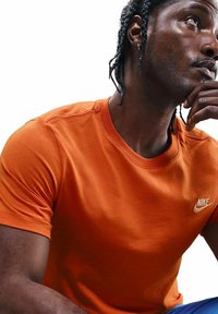 Camiseta de cuello redondo naranja hecha de algodón con un acabado texturizado, que presenta un pequeño logo blanco de Nike en el lado izquierdo del pecho.