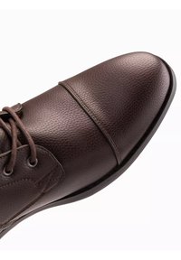 Brązowy skórzany but o teksturowanym wykończeniu, z okrągłym czubkiem, sznurowanym zapięciem i elegancką czarną podeszwą.