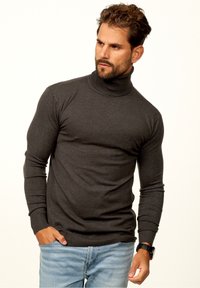 Dunkelgrauer Rollkragenpullover mit langen Ärmeln, taillierter Passform, gerippten Bündchen und Saum. Lässiger Stil kombiniert mit hellblauen Jeans.
