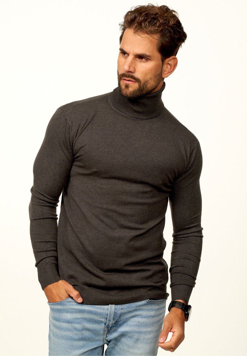 Dunkelgrauer Rollkragenpullover mit langen Ärmeln, taillierter Passform, gerippten Bündchen und Saum. Lässiger Stil kombiniert mit hellblauen Jeans.