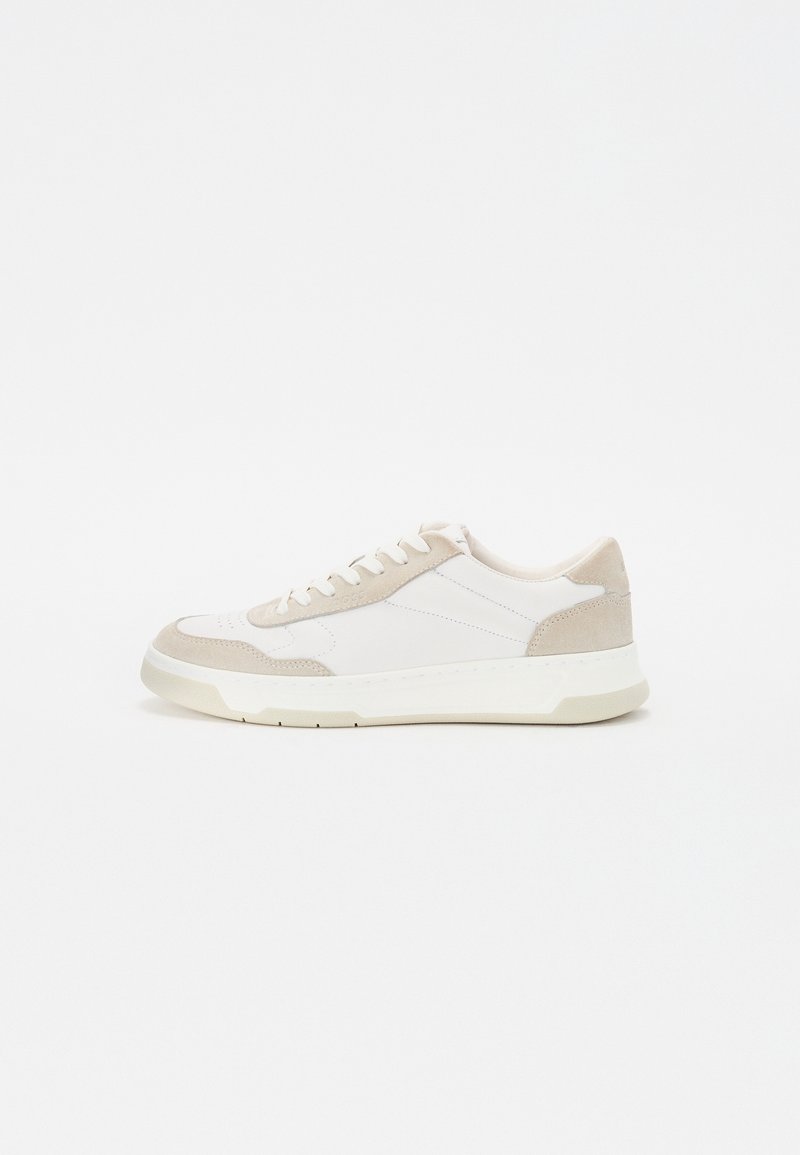 Baskets basses blanches avec des accents en daim beige, des lacets blancs et une semelle blanche épaisse sur un fond blanc uni.
