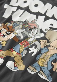 Musta T-paita, jossa on sarjakuvahahmoja hip-hop-vaatteissa, kultaketjuissa, elävissä väreissä ja painettu "Looney Tunes" -logo ylhäällä.