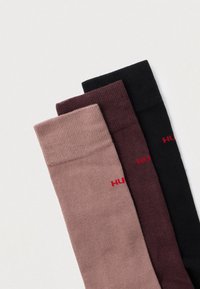 Kolm paari soonikkoes sokke pehmetest materjalidest: hele roosa, tume burgundia ja must, iga paari küljel on punase logoga märgistus.