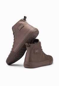 Zapatillas altas marrones hechas de material texturizado, con una suela de goma que presenta un agarre con patrón y un detalle de logotipo en el lateral.