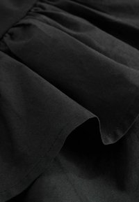 Tissu noir avec des plis rassemblés et une texture douce et lisse, montrant des coutures détaillées le long de l'ourlet.
