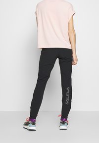 Ljusrosa kortärmad topp i kombination med svarta träningsbyxor med "SALEWA" tryckt i vitt på sidan. Sportskor med färgglada detaljer.