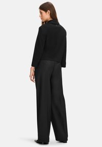 Black cropped jacket with a back button detail, paired with wide-leg black trousers. Smooth texture and tailored fit.