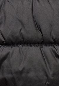Černý materiál péřové bundy s hladkou texturou, obsahující prošité části a viditelné švy. Lehký a izolační design.