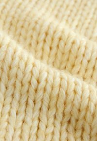 Gros plan sur un tissu tricoté épais, de couleur crème douce, avec une texture côtelée visible et des brins de fil épais.