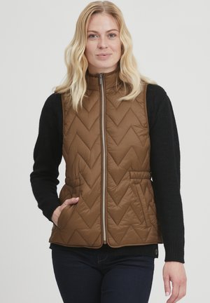 Brauner Steppwesten mit hohem Kragen und Reißverschluss vorne, mit Zickzackmuster, seitlichen Taschen und einem schwarzen Langarmpullover darunter.