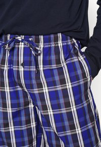 Katoenen geruite pyjamabroek met een blauw, zwart en wit kleurenschema met rode accenten; elastische tailleband en functioneel trekkoord.