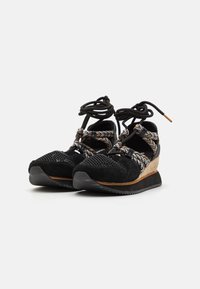 Baskets noires avec une tige texturée, des détails en maille et des lacets à motifs. Comportent une semelle en liège et en caoutchouc en forme de coin.