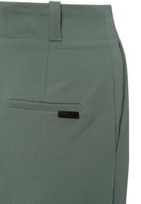 Groene op maat gemaakte broeken met een gladde textuur, voorzien van een achterzak en een zwart logo label op de tailleband.