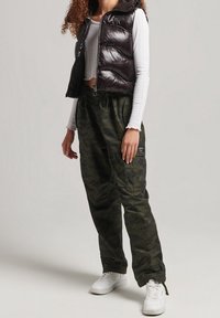 Czarna kamizelka z ociepleniem i kapturem, biały długi rękaw, oraz luźne zielone kalosze w kamuflażu. Białe sneakersy dopełniają całość.