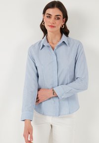 Camicia a righe azzurro chiaro e bianca con colletto, maniche lunghe e una vestibilità morbida, realizzata in un tessuto traspirante.