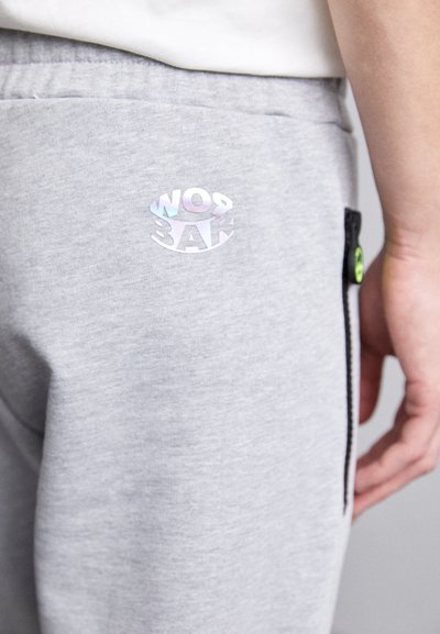 Harmaat verkkarit, joissa on heijastava logo, sivu- vetoketjullinen tasku ja sileä pinta. Korostettu vihreällä varusteella.