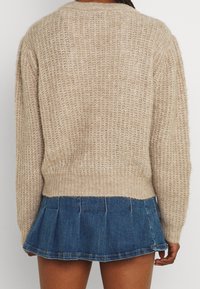 Beige knitted sweater with a textured pattern and ribbed hem, paired with a blue denim pleated skirt. Back view shows sweater's relaxed fit.