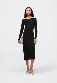 Μαύρο φόρεμα off-shoulder με μακριά μανίκια, μήκους midi, φτιαγμένο από μαλακό ύφασμα. Συνδυασμένο με μια ανοιχτή ροζ τσάντα και ανοιχτού γκρι μυτερά παπούτσια.