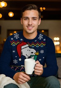Navy blue sweater with a Snoopy design, featuring snowflakes and a zigzag pattern. Holding a white mug, seated on a cozy blanket.