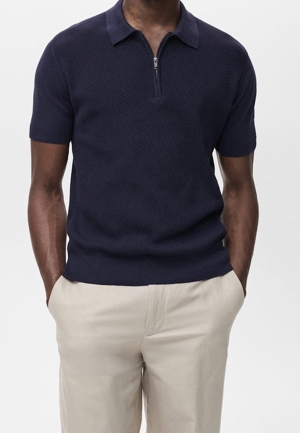 Polo manches courtes bleu marine avec un motif texturé, un col zippé et un ourlet côtelé. Associé à un pantalon beige clair.