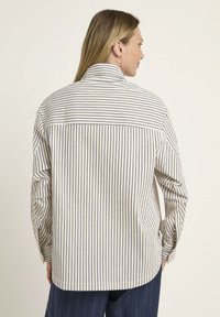 Striped button-up shirt in cream and navy cotton with a relaxed fit, featuring long sleeves and a back yoke detail for added structure.