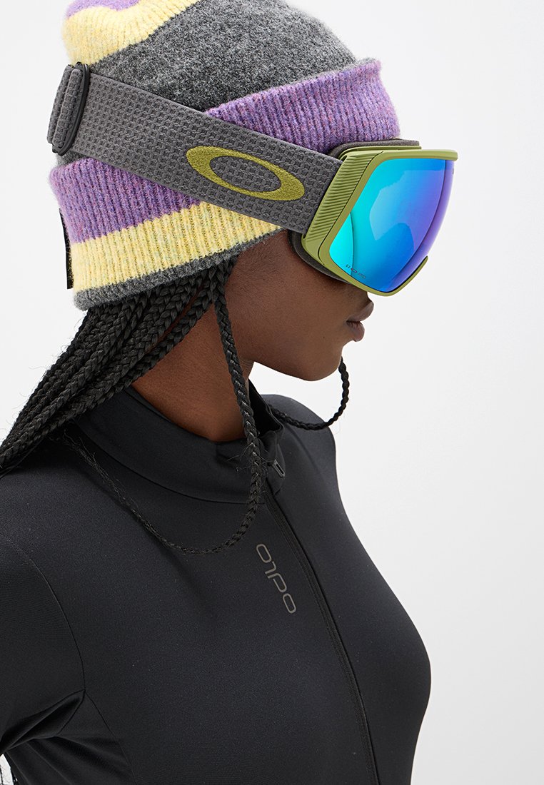Gogle narciarskie mają niebieską lustrzaną soczewkę i zieloną ramkę, noszone z wielokolorową, dzianinową czapką. Osoba ma na sobie czarną bluzę na zamek.