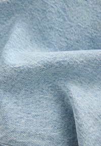 Šviesiai mėlynas džinsinis audinys, rodantis smulkias įstrižas audimo lignes, lygų paviršių ir nedidelį elastingumą, turintis švelnų, neformalus išvaizdą.