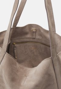 Sac fourre-tout en daim taupe avec poche intérieure zippée et double bandoulières, doté d'une fermeture éclair et d'un anneau de couleur or.