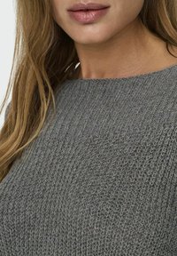 Maglione grigio lavorato a maglia con una texture a coste e un colletto rotondo, che presenta una vestibilità morbida e rilassata. Primo piano dei dettagli del tessuto.