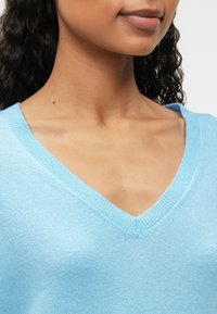 Világoskék V nyakú pulóver bordázott szélekkel, puha textúrával és laza szabással, semleges háttér előtt bemutatva.