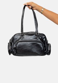 Bolso de cuero negro con dos asas resistentes, cierre de cremallera y un bolsillo frontal. Presenta lados redondeados y una textura suave y brillante.