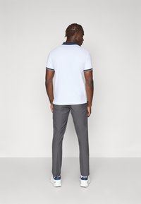 White polo shirt with navy accents, short sleeves, paired with gray trousers and white athletic shoes. Rear view, simple design, no patterns.