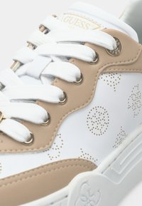 Sneaker bianca con accenti beige, caratterizzata da motivi perforati rotondi, occhielli in metallo dorato e lacci bianchi, realizzata in materiale sintetico.