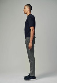 Sort bomulds T-shirt, grå slim-fit bukser og sorte sneakers. Modellen står i profil mod en neutral baggrund.
