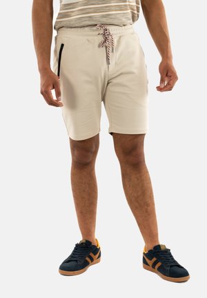 Shorts beiges avec une taille élastique et un cordon de serrage rayé, dotés de poches zippées noires et d'une texture lisse et douce.