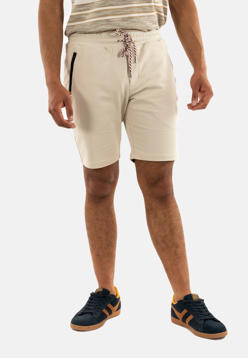 Shorts beiges avec une taille élastique et un cordon de serrage rayé, dotés de poches zippées noires et d'une texture lisse et douce.