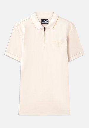 Beige polo shirt with short sleeves, zipper neck, and subtle logo embroidery. Soft fabric with contrasting neck and sleeve accents.