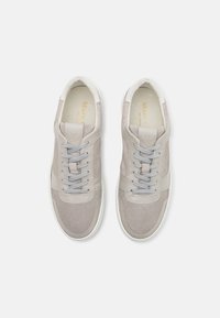 Zapatillas de color gris claro con materiales de ante y cuero, cordones planos grises y una suela de goma blanca. Presenta acentos laterales y un logotipo embosado.