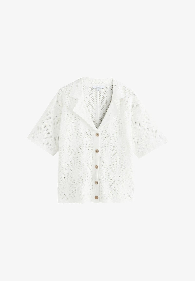 Bluza albă din dantelă cu mâneci scurte, margini ondulate, guler și cinci nasturi din lemn pe partea din față.